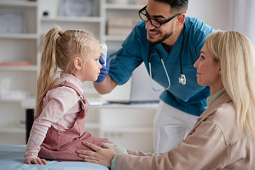 A mother holding a child whilst a GP takes their temperature