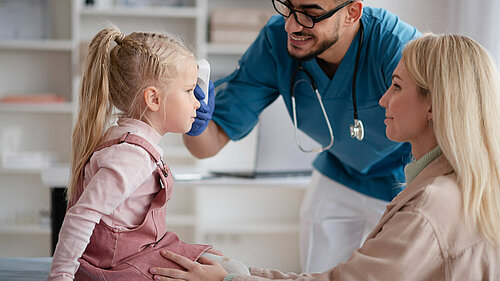 A mother holding a child whilst a GP takes their temperature